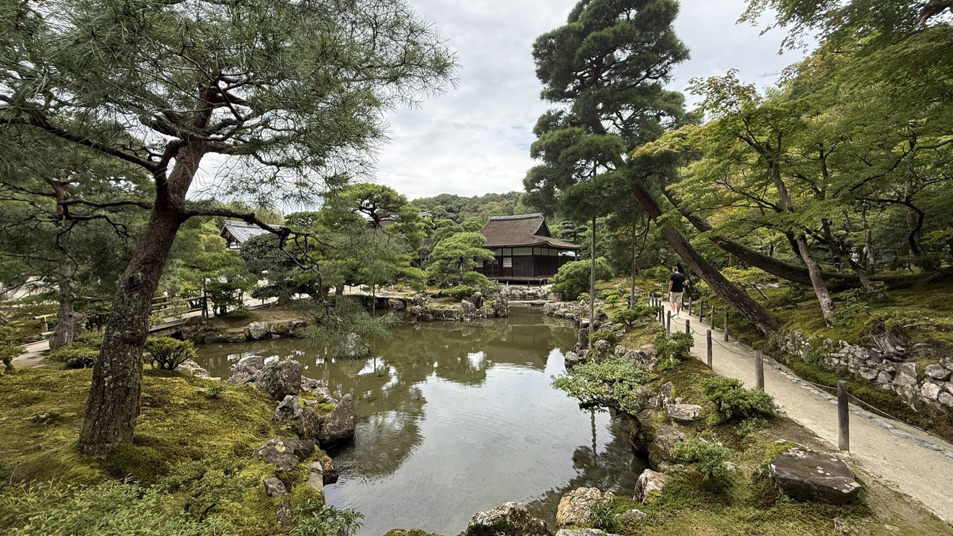 銀閣寺觀音殿深色木造二層建築,白牆黑瓦,周圍是水池與松樹