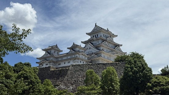 從外苑公園遠望姬路城天守閣,白色城樓在綠樹與藍天之間清晰可見