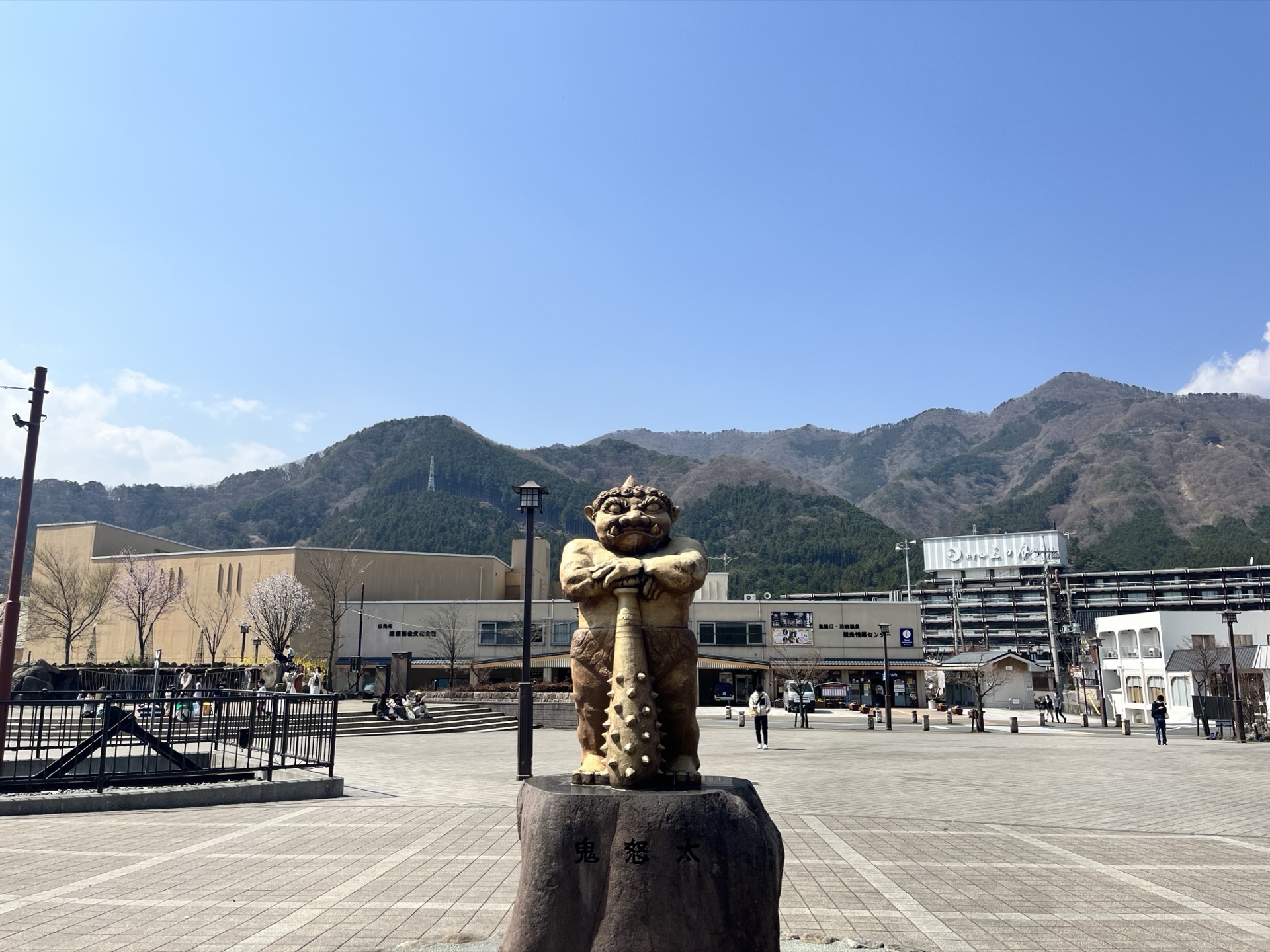 鬼怒川溫泉站前廣場,前景是手持棒槌的鬼怒太青銅雕像,背景為群山與溫泉旅館街