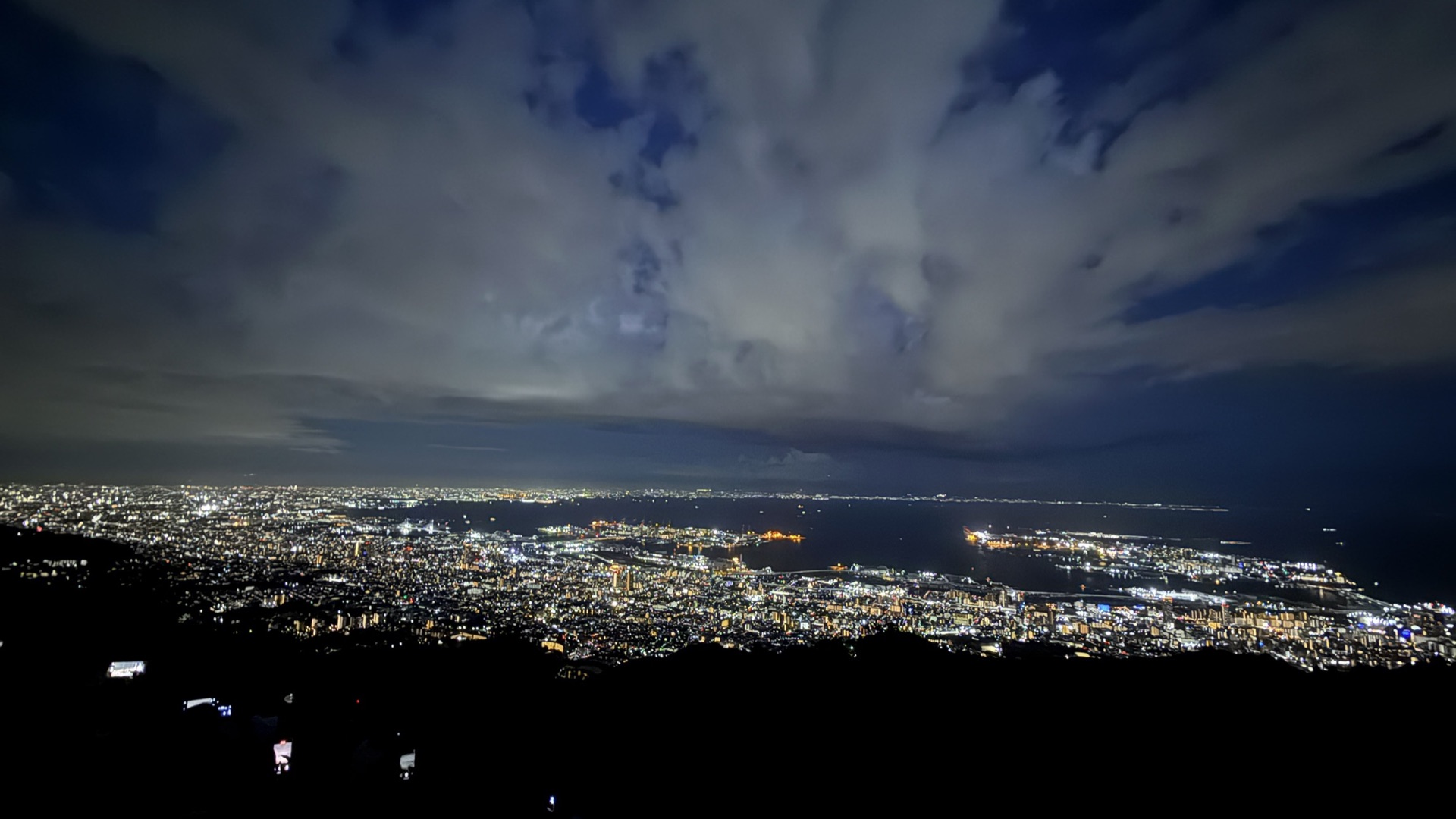 從摩耶山掬星台俯瞰的大阪灣夜景全景，烏雲後方透出城市燈光，視野遼闊